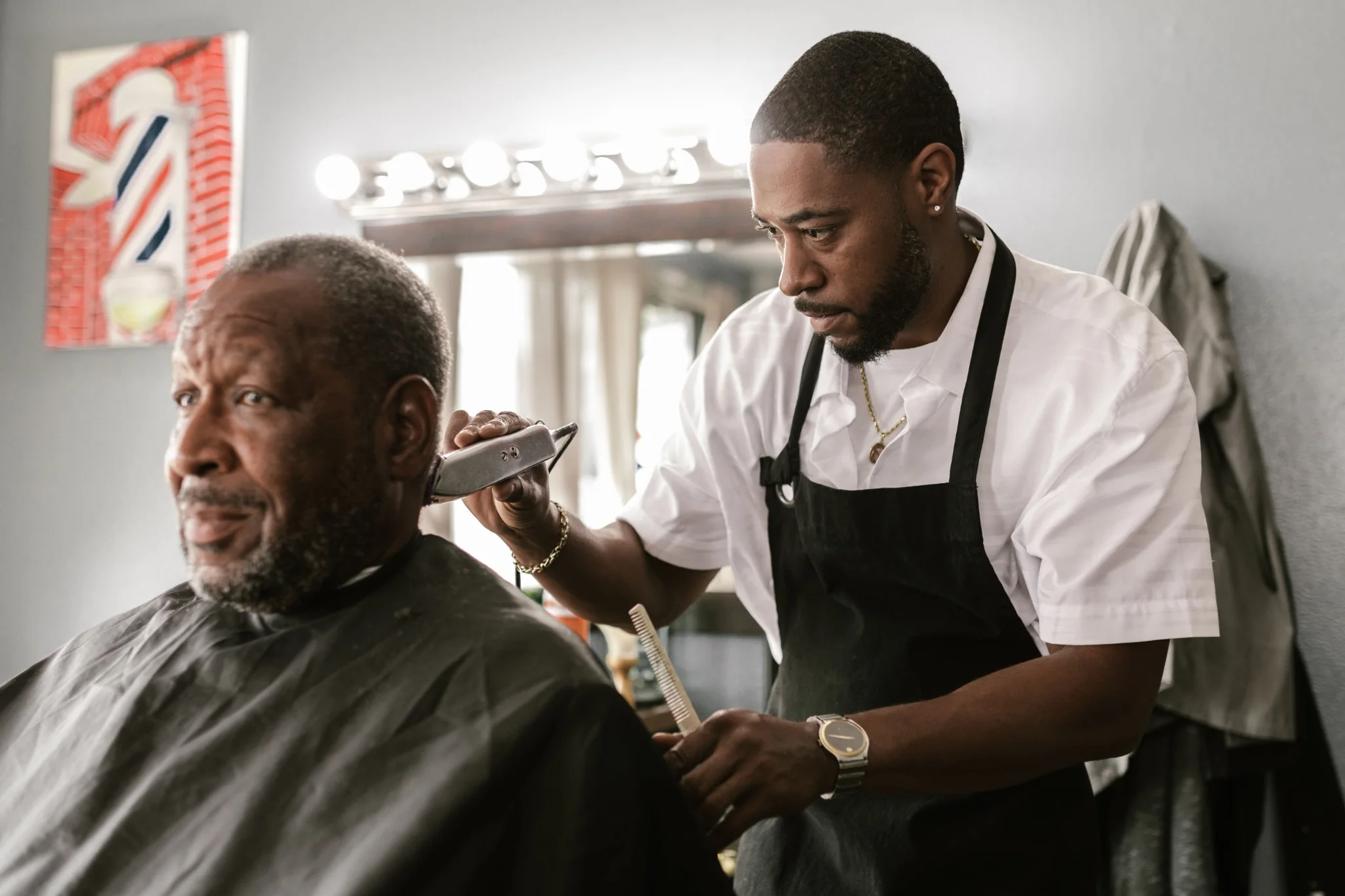 Barber trimming an older client's hair in a professional barber workspace.