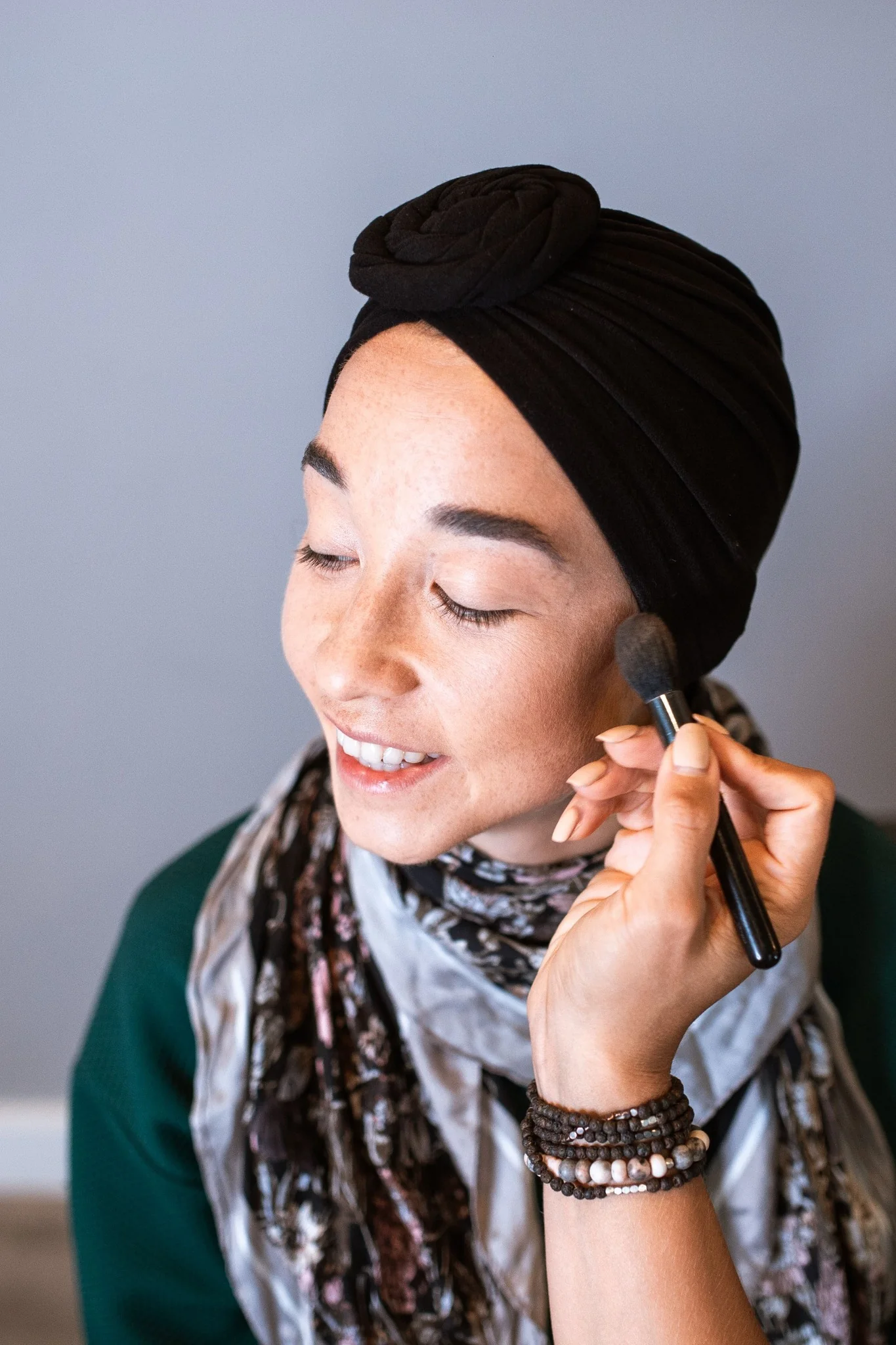 Client applying makeup while wearing a black headwrap
